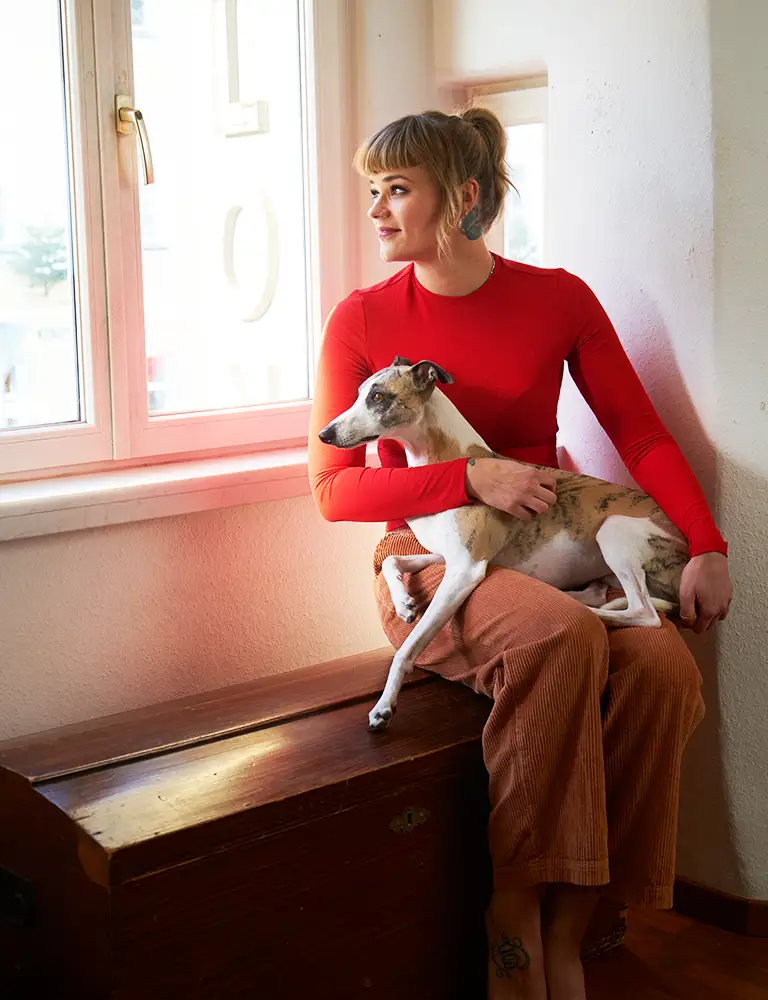 Frau mit Morbus Crohn sitzt mit ihrem Hund am Fenster.