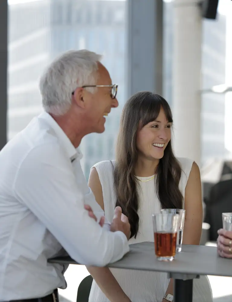 Drei Mitarbeitende tauschen sich auf der Dachterrasse aus und lachen sich an. 